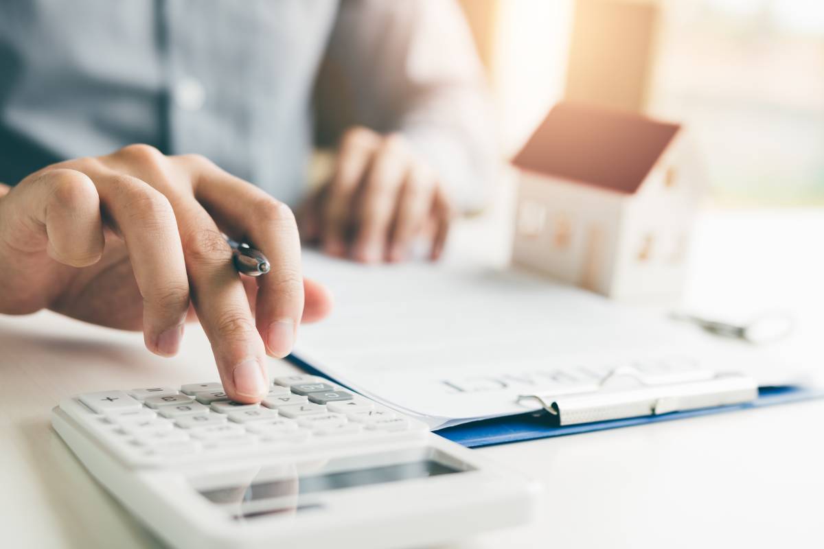 Person calculating home or property expenses with a calculator and house model on desk.